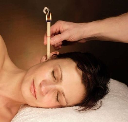 A woman receiving ear candling treatment in a comfortable massage environment setting.