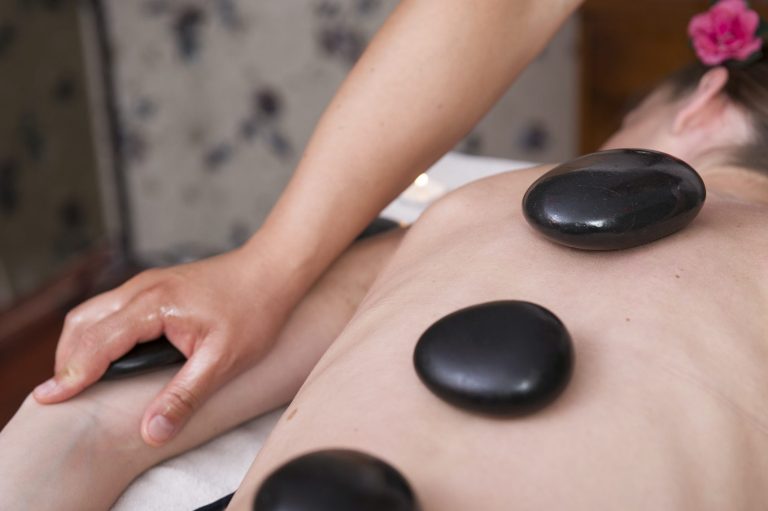 A person receiving a hot stone massage with smooth black stones on their back.